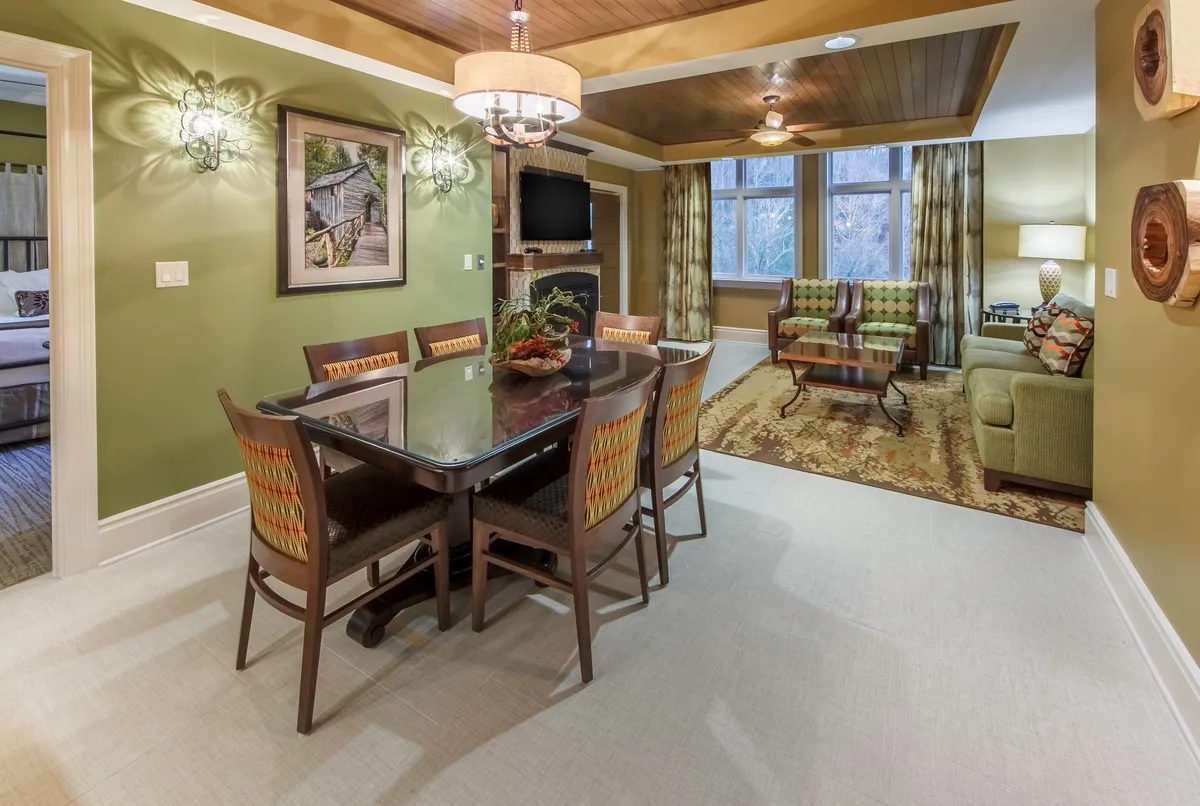 A cozy living/dining space featuring a comfortable sofa, dining table, distinctive wall art, and expansive windows letting in daylight. The intimate arrangement invites families to gather for meals, games, or quiet evenings together.