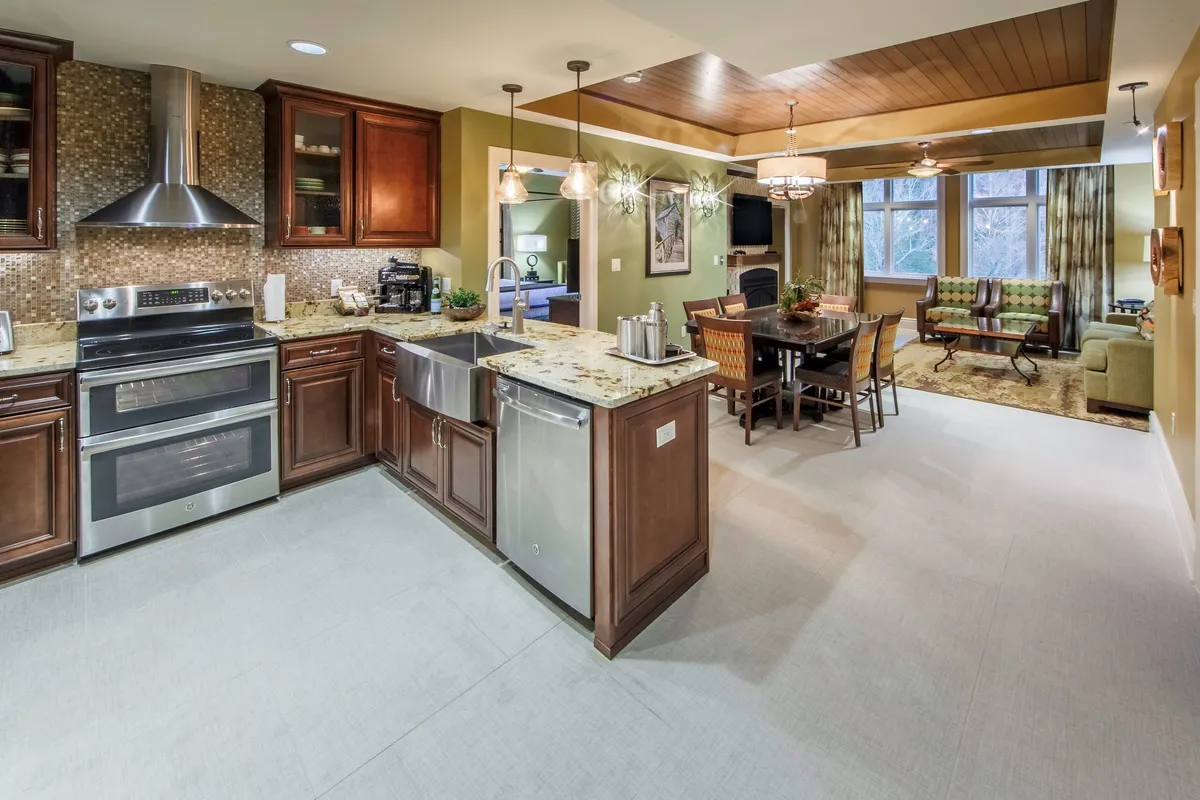 A spacious open-plan living area with a kitchen island, dining table, and inviting seating area, all illuminated by large windows. The room looks ideal for socializing, entertaining, and relaxing, and exudes a warm, welcoming vibe.
