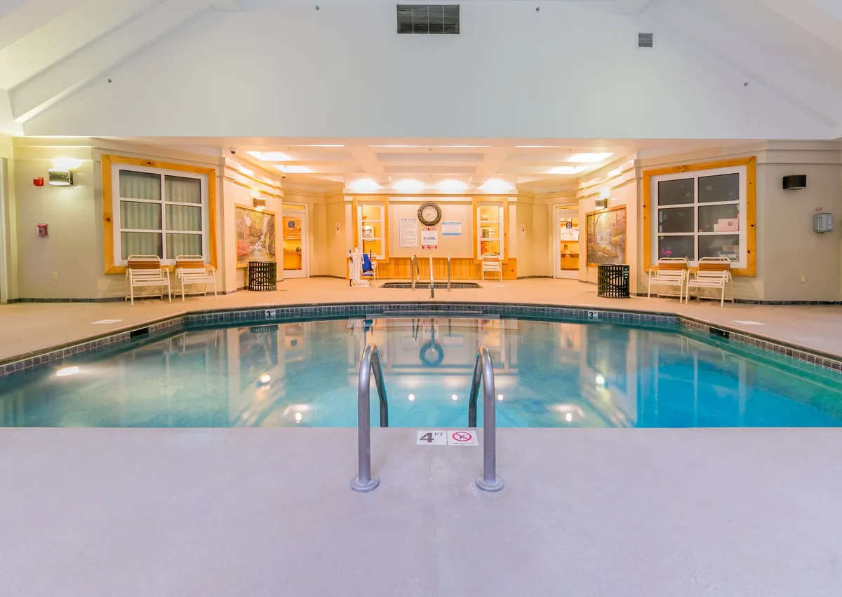 A sleek indoor pool area with inviting poolside seating and a welcoming reception space. Guests are depicted swimming, relaxing by the pool, and socializing, with the ambiance set by gentle natural light and a sense of comfort and leisure.